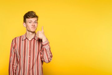 approving smiling man showing a thumb up gesture. portrait of a young guy on yellow background....