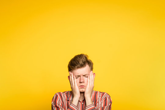 sad rueful depressed cheerless man covering his face in hands. portrait of a young guy on yellow background popping up or peeking out from the bottom. copyspace for advertisement.