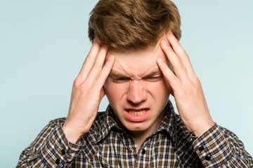 headache or migraine. man in pain clutching his head. discomfort ache and misery. portrait of a young guy on light background. emotion facial expression. feelings and people reaction concept.