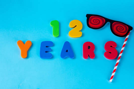 12 years old celebrating classic logo.Cute Masquerade Masks glasses on Stick. Colored happy anniversary 12 th  numbers on blue background. Greetings celebrates card.Traditional digits of ages.Top view