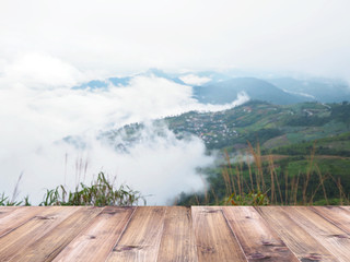 Wood table top over green mountain with white fog background.