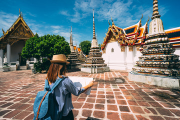 Fototapeta premium Young woman traveler with backpack and hat looking the Map in Wat Pho at Bangkok Thailand. Traveling in Bangkok Thailand