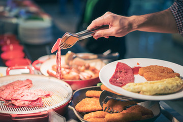 Man hand pick ham or bacon into plate in breakfast at hotel