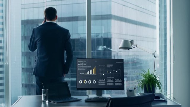 Confident Businessman in a Suit Standing in His Office, Looking out of the Window and Making Important Phone Call so He can Close the Deal. 