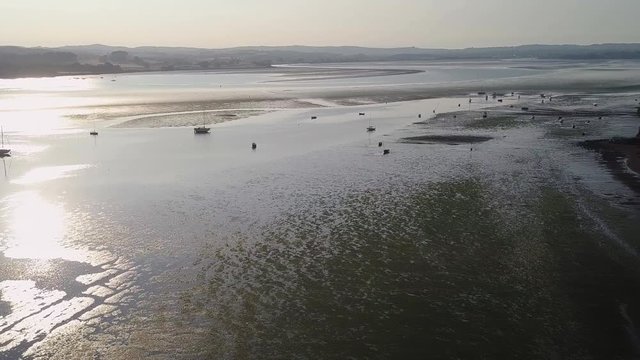 Flying over docked ships and sailing boats off of the beach in Lympstone England. The boats and ships are silhouettes against the evening sunset. The area looks amazingly peaceful.