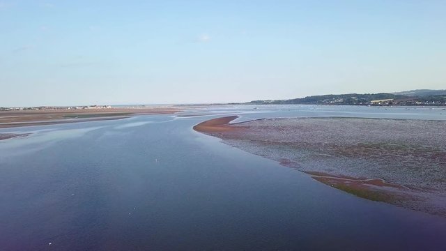 Flying over the coastal town of Lympstone England. In the distance boats are docked close to shore. Water plants such as water grass is visible in the video.