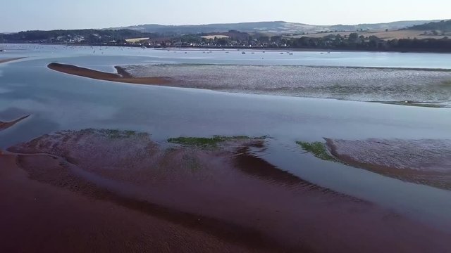 Harbour town view from the sky. Flying over the ocean off of the coast of Lympstone England. Land and the town is seen in the distance, the water has water plants.