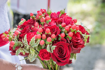 Beautiful bouquet of a bride with red roses close-up on a walk of the newlyweds in the park
