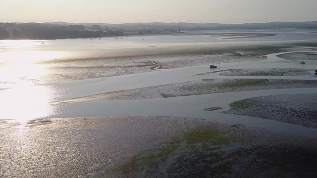 Gliding over the oceans water off of the shores with sail boats docked and silhouetted against the reflection of the evening glow in the water. The water is calm and the landscape peaceful.