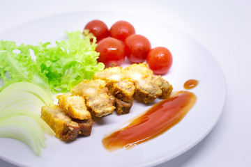 Fried pork meat on white dish with vegetable side dishes and spicy sauce