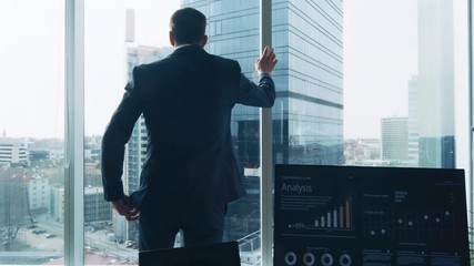Following Shot of the Confident Businessman in a Suit Walking Through His Office and Looking out of the Window Thoughtfully. Stylish Modern Business Office with Personal Computer and Big City View. - Powered by Adobe