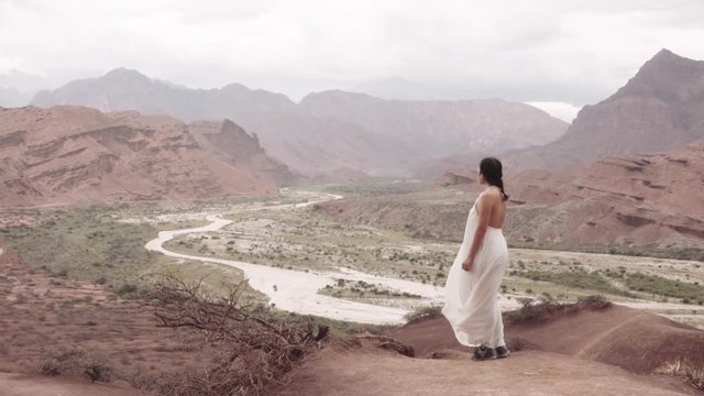 Woman wearing bride dress stands contemplating the canyon landscape