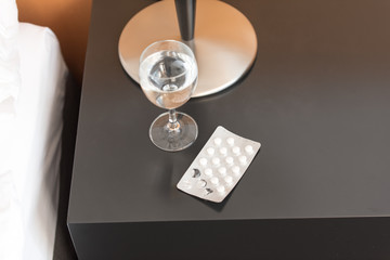 Wasserglas mit Tabletten auf dem Nachttisch am Bett