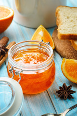 orange jam in glass jar and ingredients on blue background