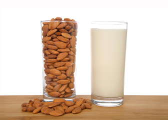 Glass of almond milk next to glass of whole almonds on a wood table with raw almonds, isolated on white background. Almond milk is lower in calories than other milks. cholesterol free, lactose free.