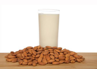 Glass of almond milk on a wood table surrounded by whole raw almonds, isolated on white background. Almond milk is lower in calories than other milks and cholesterol free, lactose free.