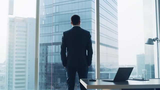 Back View of the Thoughtful Businessman wearing a Suit Standing in His Office, Hands in Pockets and Contemplating. Shot on RED EPIC-W 8K Helium Cinema Camera.