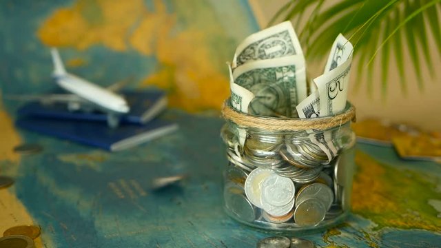 Travel budget concept. Money saved for vacation in glass jar with world map, passport and plane. Banknotes and coins for adventure. Savings for journey. Collecting money for trip. Moneybox with cash.