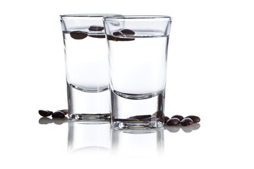 Two shot glasses with Italian Sambuca hard liquor surrounded by coffee beans isolated on white...