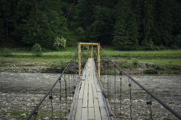 Old pedestrian hanging bridge over river in the mountains