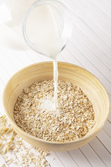 Oatmeal flakes in a wooden bowl on a white background. Milk pours into a bowl of cereal. Vertically.