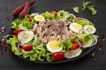 Salad with tuna, anchovies and vegetables. Mediterranean food. The background is black. Top view. Copy space. Horizontal shot.