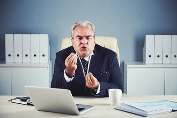 Furious mad elderly male in business suit sitting at office workplace with laptop emotionally...