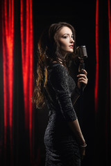 Young beautiful singer in black dress posing with microphone