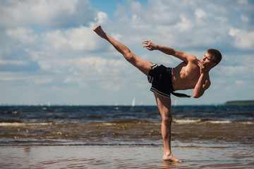 Fototapeta premium Kickboxer kicks in the open air in summer against the sea.