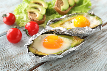 Baked avocado with eggs and vegetables on wooden background