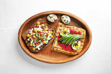 Plate with tasty toasts on light background