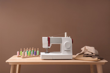 Modern sewing machine, set of threads and fabric on table against color background