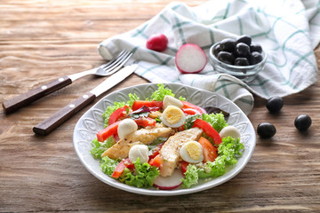 Tasty chicken salad with vegetables and quail eggs in bowl on wooden table