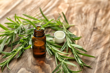 Fresh rosemary and bottle of essential oil on wooden background