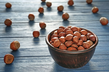Bowl with tasty hazelnuts on wooden background