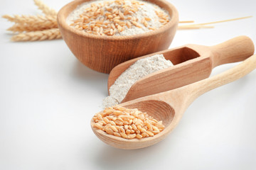Spoon with wheat grains and scoop with flour on white background