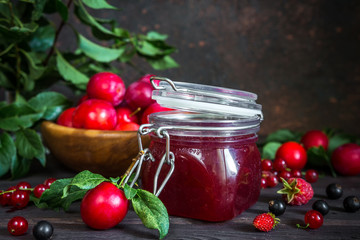 assortment of jam in glass jars, seasonal fresh berries and fruit plum, strawberry, currant, raspberries on a dark background selective focus with copy space, crop concept