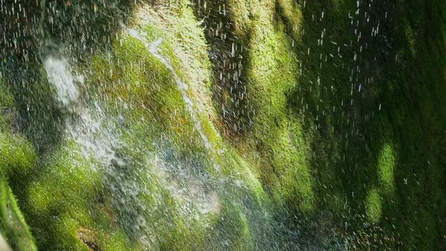 SLOW motion, waterfall in mountains in high speed reel. Closeup of spring water drops falls and splashing on green moss