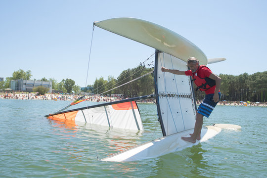 salior trying to right his catamaran after capsize