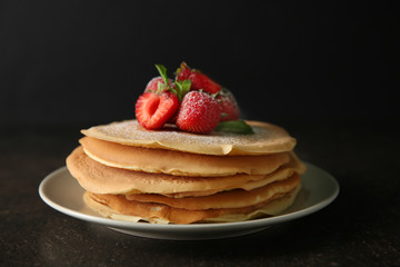Plate with delicious pancakes and strawberries on table against dark background
