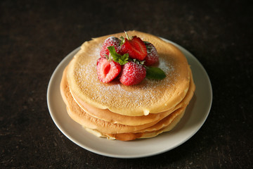 Plate with delicious pancakes and strawberries on dark table