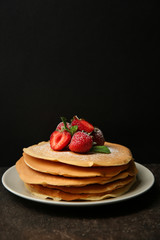 Plate with delicious pancakes and strawberries on table against dark background