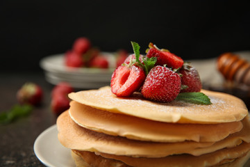 Plate with delicious pancakes and strawberries on table against dark background, closeup