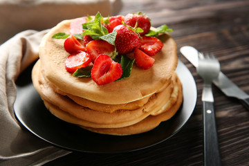 Plate with delicious pancakes and strawberries on wooden table, closeup