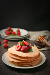 Plate with delicious pancakes and strawberries on table against dark background