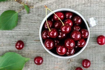 Cherries in aluminum cup on wooden background. Harvesting berries, rustic style.