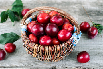 Ripe purple plums in basket on wooden background.