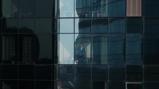 Aerial View Footage: From Outside into Office Building with Businessman Working and Looking out of the Window. Beautiful Flying Zoom Out Shot of The Financial Business District Skyscrapers. 