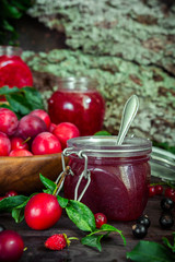 assortment of jam in glass jars, seasonal fresh berries and fruit plum, strawberry, currant, raspberries on a dark background selective focus with copy space, crop concept