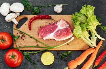 Fresh beef steak, wooden spoon, Assortment of Fresh Vegetables, aromatic herbs, spices and vegetables for cooking , on black  background, top view. Meat